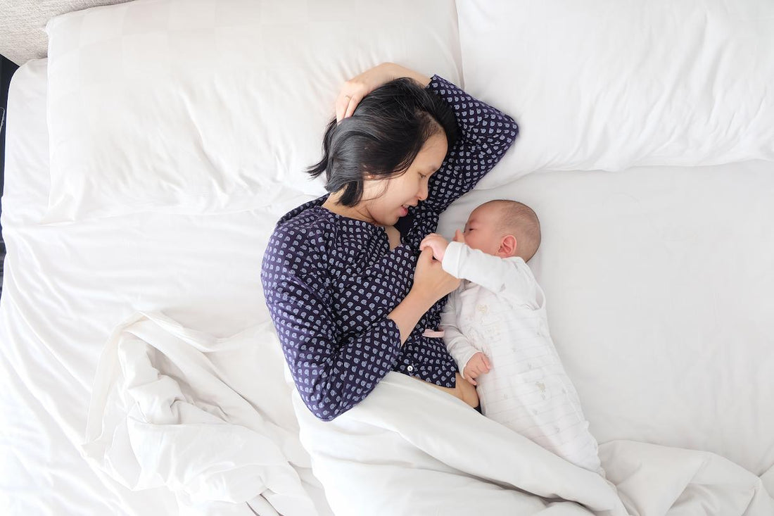 Mum lying on a white bed cuddling her baby