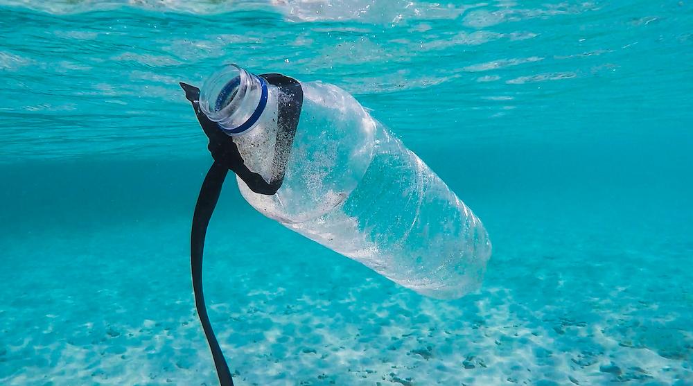 plastic bottle waste floating in clear blue waters with sandy seabed
