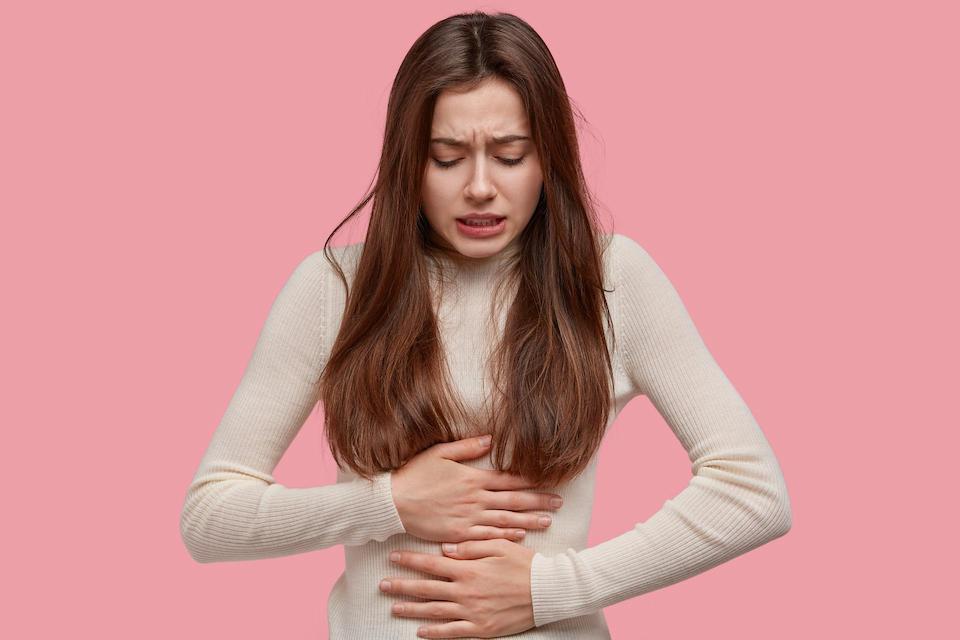 Woman holding stomach with period pain, pink background, NORA period wear, blog post